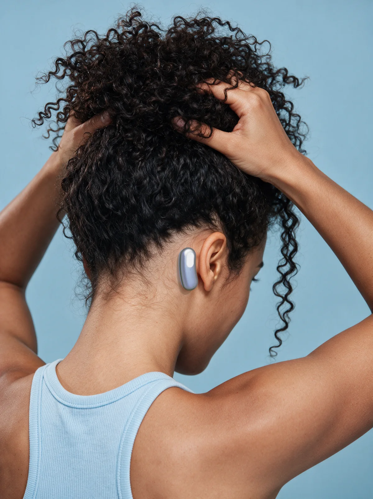 A person lifts their curly hair to reveal Brane behind the ear against a blue background