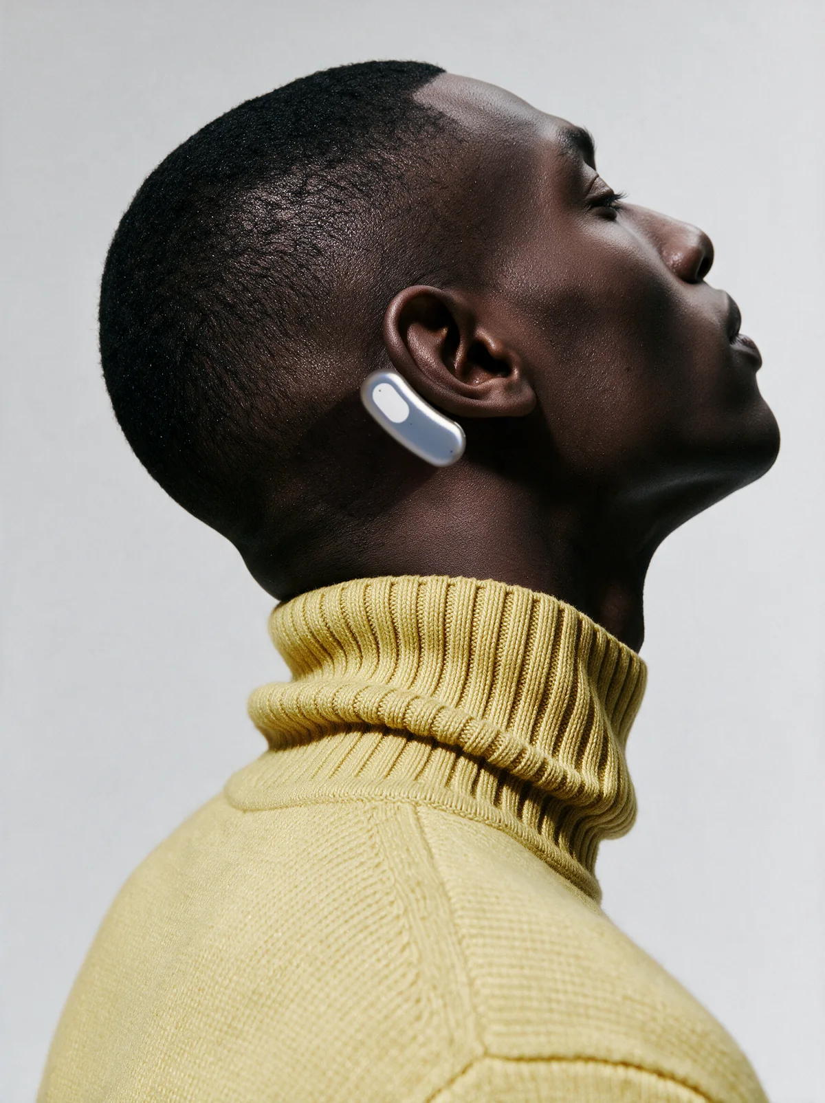 A person in a pale-yellow knit top wearing Brane behind the ear, seen in profile